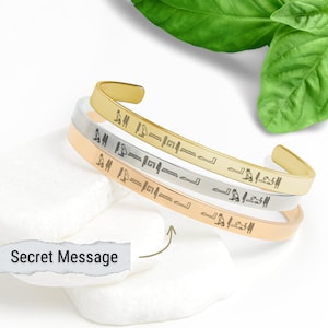 May include: Three gold, silver, and rose gold bracelets with a secret message engraved on each. The bracelets are stacked on top of each other.