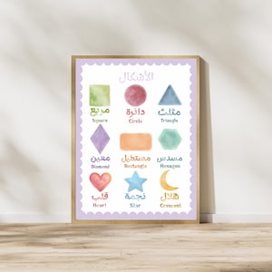 May include: A framed educational wall art print featuring nine watercolor shapes in various colors. Each shape is labeled with its name in both Arabic and English text. The shapes include a square, circle, triangle, diamond, rectangle, hexagon, heart, star, and crescent, all arranged on a white background with a scalloped light purple border.