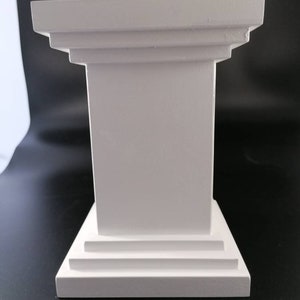 May include: White pedestal with a square top and a base with three steps. The pedestal is made of a smooth, white material.