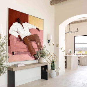 May include: Large abstract painting featuring a figure in a white shirt and brown pants reclining on a pink sofa. The background is divided into red and gold sections. The artwork is displayed in a bright, modern interior.