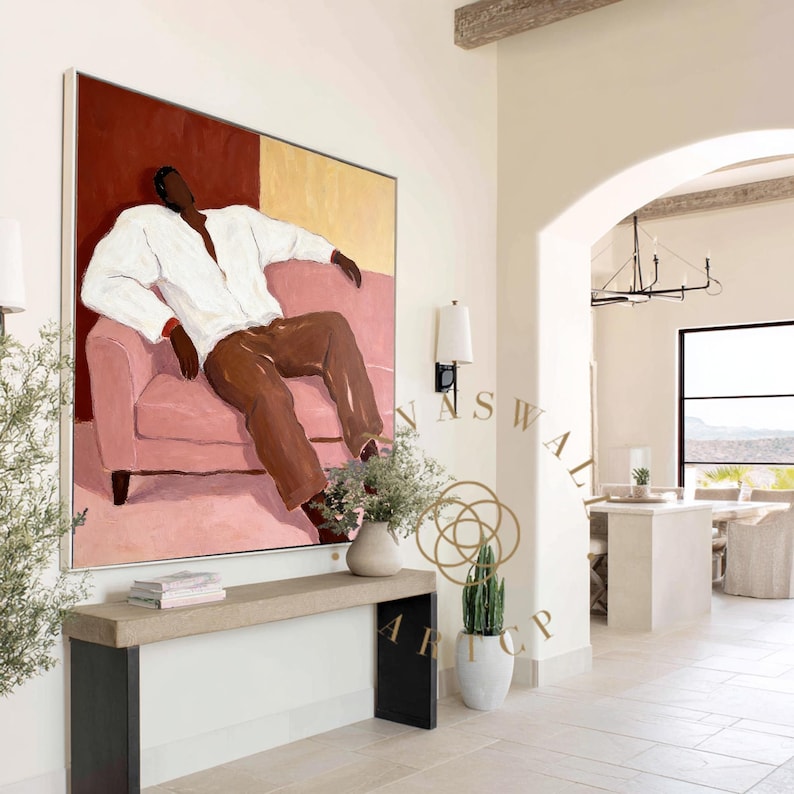 May include: Large abstract painting featuring a figure in a white shirt and brown pants reclining on a pink sofa. The background is divided into red and gold sections. The artwork is displayed in a bright, modern interior.
