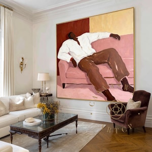 May include: Large framed painting featuring a figure reclining on a pink sofa. The figure wears a white shirt and brown pants. The background is divided into red and yellow sections. The artwork is displayed in a living room setting.