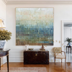 May include: Large abstract painting with a textured surface, featuring horizontal bands of color that transition from light beige at the top to deep blue at the bottom. The artwork is framed in gold and hangs in a well-lit room.