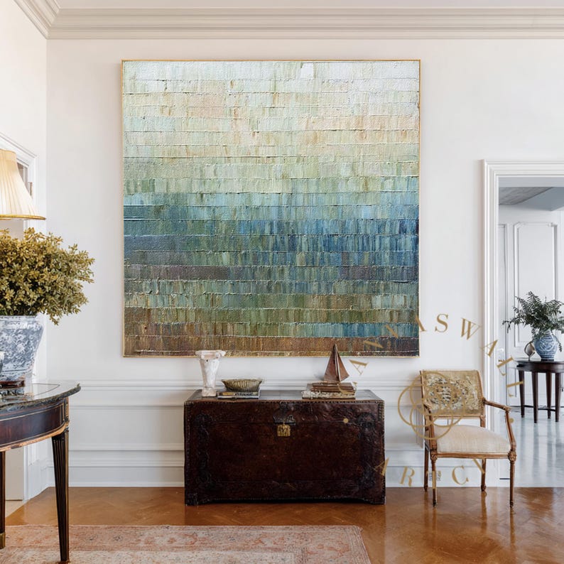 May include: Large abstract painting with a textured surface, featuring horizontal bands of color that transition from light beige at the top to deep blue at the bottom. The artwork is framed in gold and hangs in a well-lit room.