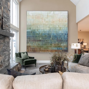 May include: Large abstract painting with a textured surface, featuring horizontal bands of color that transition from light beige at the top to shades of blue and green at the bottom. The artwork is framed in a silver metal.