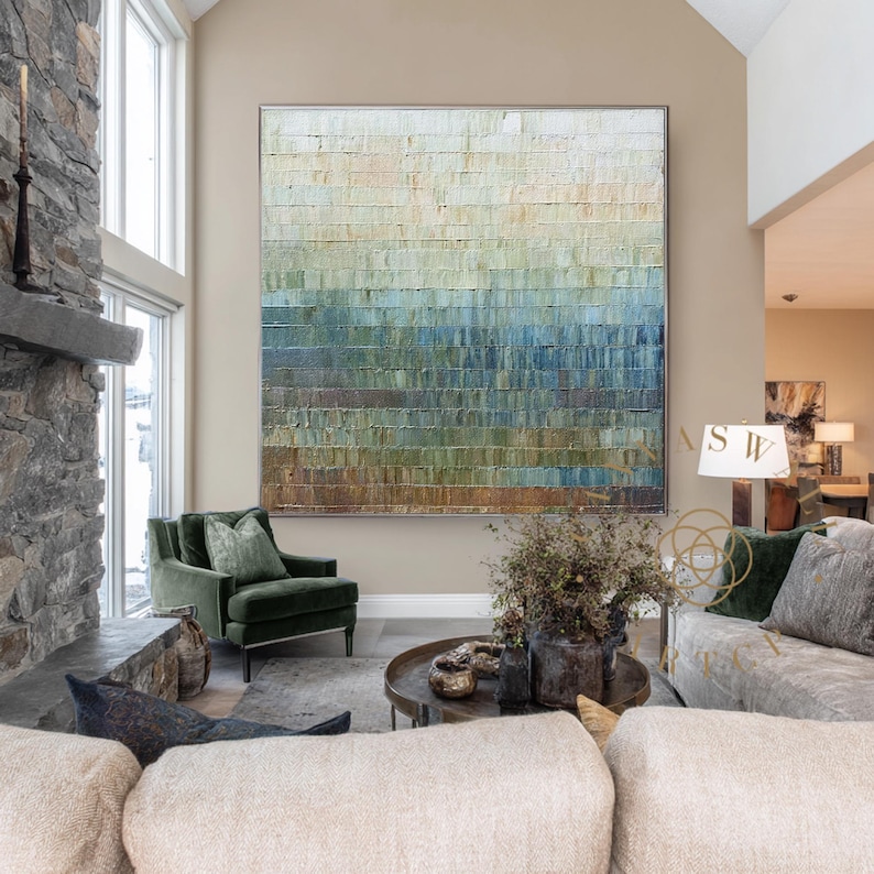 May include: Large abstract painting with a textured surface, featuring horizontal bands of color that transition from light beige at the top to shades of blue and green at the bottom. The artwork is framed in a silver metal.