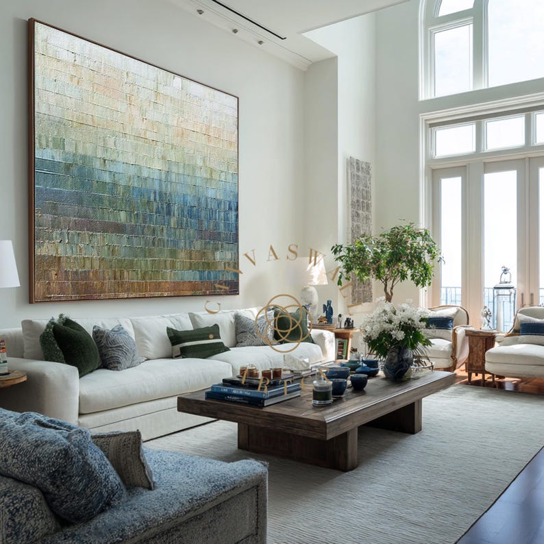 May include: A large, abstract painting in a living room setting. The artwork features a textured, rectangular design with horizontal bands of color, transitioning from brown to blue and green. The room includes a white sofa, coffee table, and decorative pillows.