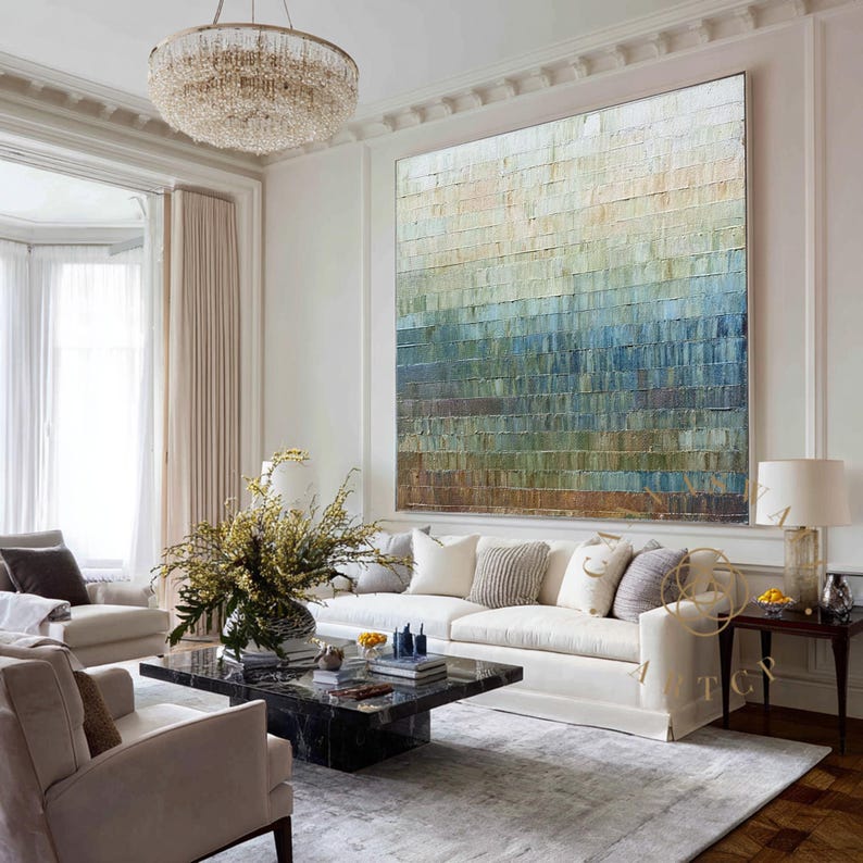 May include: Large abstract painting with a textured surface, featuring a gradient of colors from beige to blue and brown. The artwork hangs above a white sofa in a well-lit living room, with a chandelier and a black marble coffee table.