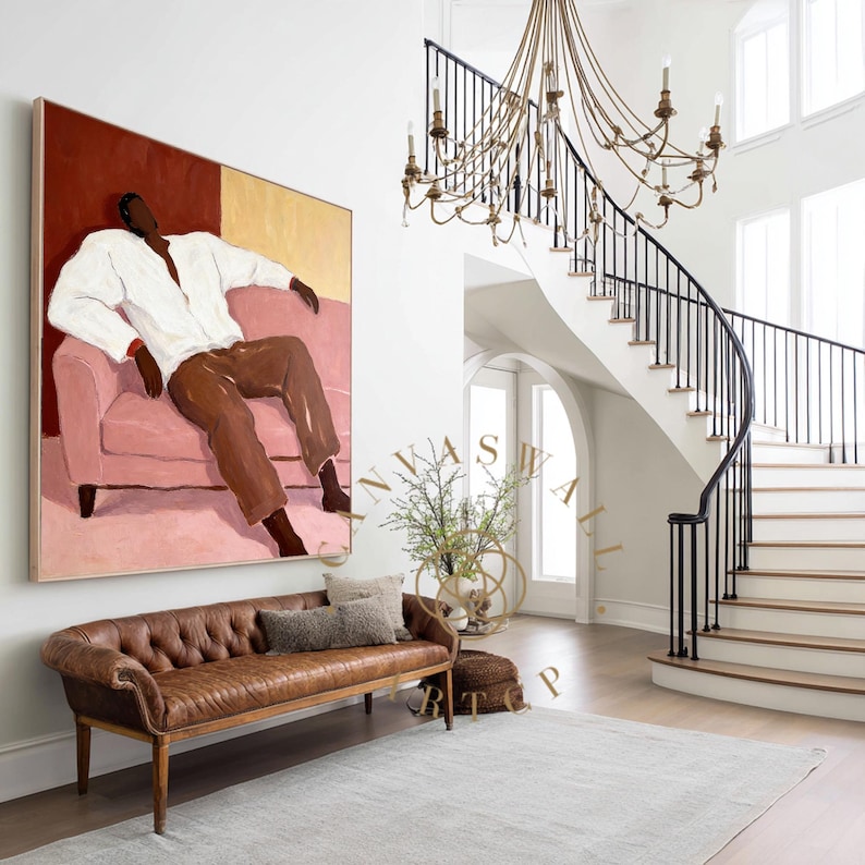 May include: An abstract painting of a person in a white shirt and brown pants seated on a pink sofa. A brown leather bench with pillows sits below the painting. A staircase with a black railing and a chandelier are in the background.