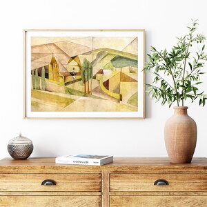 Peut inclure: Une peinture &agrave; l'aquarelle encadr&eacute;e d'un paysage avec une maison jaune et des arbres verts. La peinture est dans un cadre en bois clair et est accroch&eacute;e &agrave; un mur blanc. Il y a un vase avec une plante verte et un bol d&eacute;coratif sur une commode en bois.