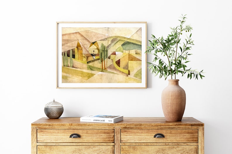 Peut inclure: Une peinture &agrave; l'aquarelle encadr&eacute;e d'un paysage avec une maison jaune et des arbres verts. La peinture est dans un cadre en bois clair et est accroch&eacute;e &agrave; un mur blanc. Il y a un vase avec une plante verte et un bol d&eacute;coratif sur une commode en bois.