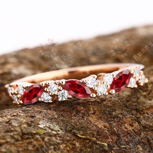 May include: A rose gold band ring with a delicate design featuring alternating marquise-shaped red rubies and round white diamonds.