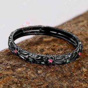 May include: A black ring with a floral design and small pink and green gemstones.