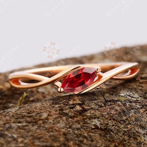 May include: A rose gold ring featuring a marquise-shaped red gemstone set in a delicate, twisted band.