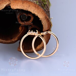 May include: Two gold rings with small clear stones set in the band. The rings are interlocked and are sitting on a piece of wood.