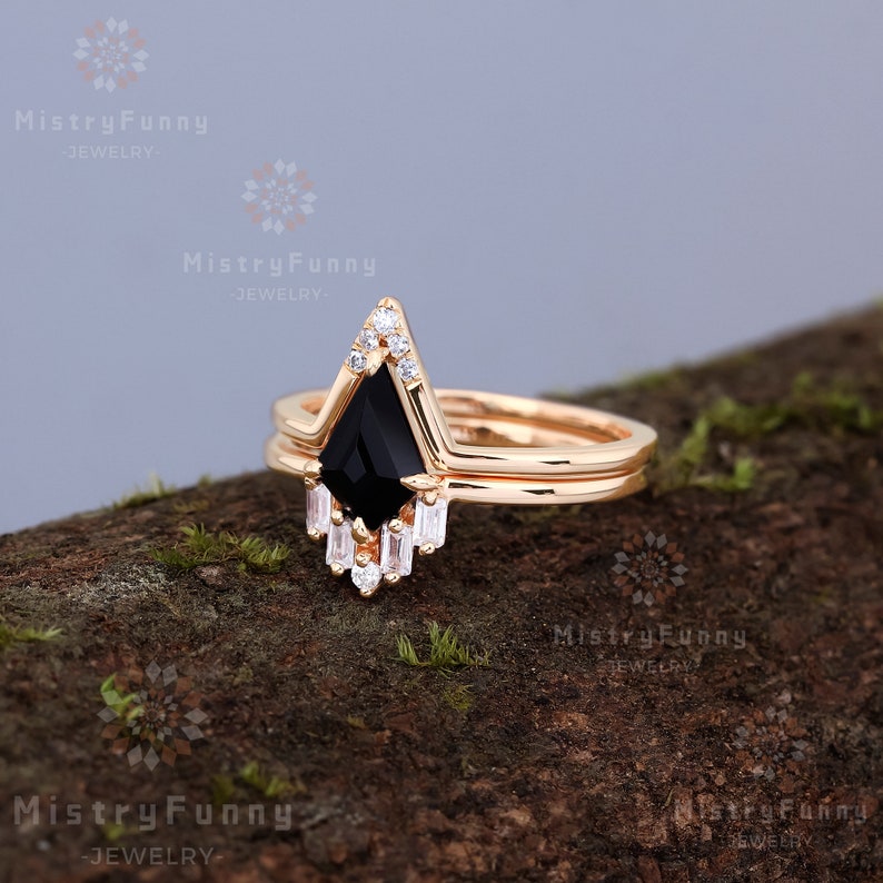 May include: A gold ring set with a black pear-shaped gemstone and smaller clear gemstones. The ring is on a wooden surface.