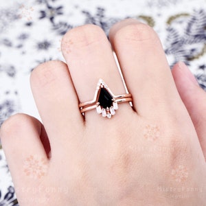 May include: A three-piece rose gold engagement ring set with a black pear-shaped center stone and a halo of small round diamonds. The band is accented with baguette-shaped diamonds.