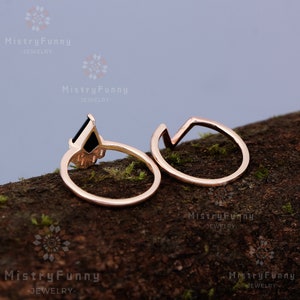 May include: Two gold rings, one with a black gemstone and a geometric design, the other a simple circle with a geometric design.