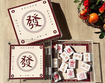 May include: A set of Mahjong tiles and boxes. The boxes are white with red trim and Chinese characters. The tiles are white with red characters and images. The set is displayed in a clear acrylic case. The boxes have the Chinese character "Fa" in the center.