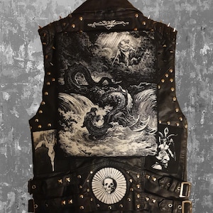May include: Black leather vest with a detailed graphic print on the back depicting a mythological scene. The vest features metal studs, spikes, and decorative patches. Buckles and a skull emblem add to the edgy design.