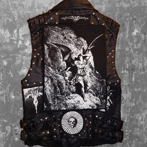 May include: Black leather vest with metal studs and a large graphic on the back featuring a winged figure. Additional patches and a skull emblem are visible. The vest has a classic biker style.