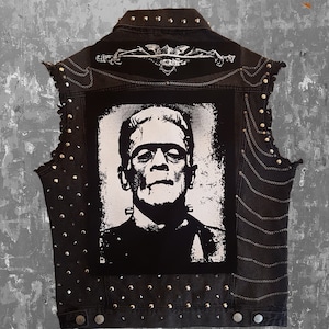 May include: Black denim vest with silver studs and a black and white Frankenstein patch on the front.