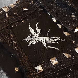 May include: Black denim jacket with silver pyramid-shaped studs and a white embroidered patch of a winged creature on the front.