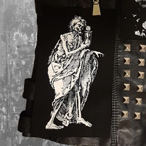 Könnte beinhalten: Schwarze Lederjacke mit einem Skelett, das eine Sanduhr hält, einem Nietenpanel und einem Reißverschluss.