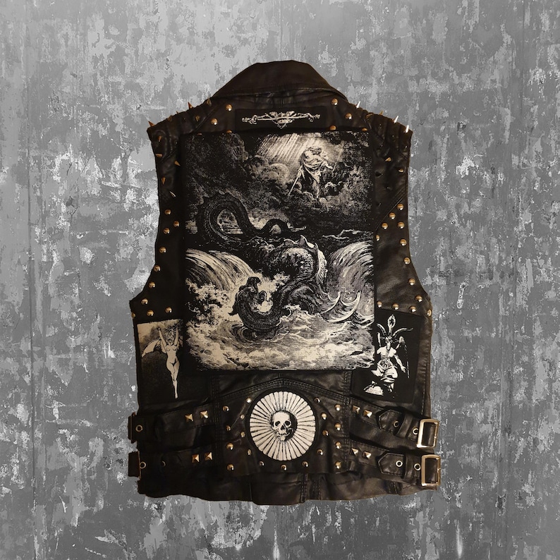 Pode incluir: Colete de couro preto com uma estampa gr&aacute;fica detalhada nas costas retratando uma cena mitol&oacute;gica. O colete apresenta tachas de metal, pontas e patches decorativos. Fivelas e um emblema de caveira.