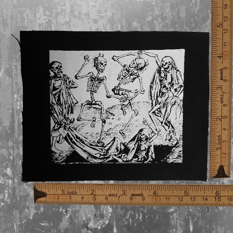 May include: Black and white embroidered patch featuring a scene of five skeletons dancing. The patch is sewn onto a black fabric background.