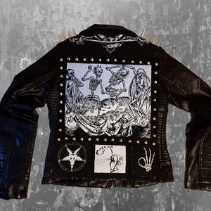 Peut inclure: Veste en similicuir noire avec des clous et des pointes dorées. Le dos présente un grand motif en noir et blanc de squelettes dansant, avec de plus petits écussons de symboles et une main de squelette.