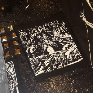 Puede incluir: Parche blanco y negro con el texto "In The Wake Of The Thord" en una fuente gótica. El parche presenta un gráfico de una escena con múltiples figuras.