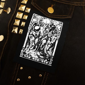 May include: Black and white patch with a detailed illustration of a figure with a crown and a staff, surrounded by other figures. The patch is sewn onto a black denim jacket with gold studs.