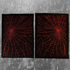 K&ouml;nnte beinhalten: Zwei schwarze Stoffbahnen mit einem roten Spinnennetz-Design. Die Bahnen liegen nebeneinander und haben eine raue Textur.