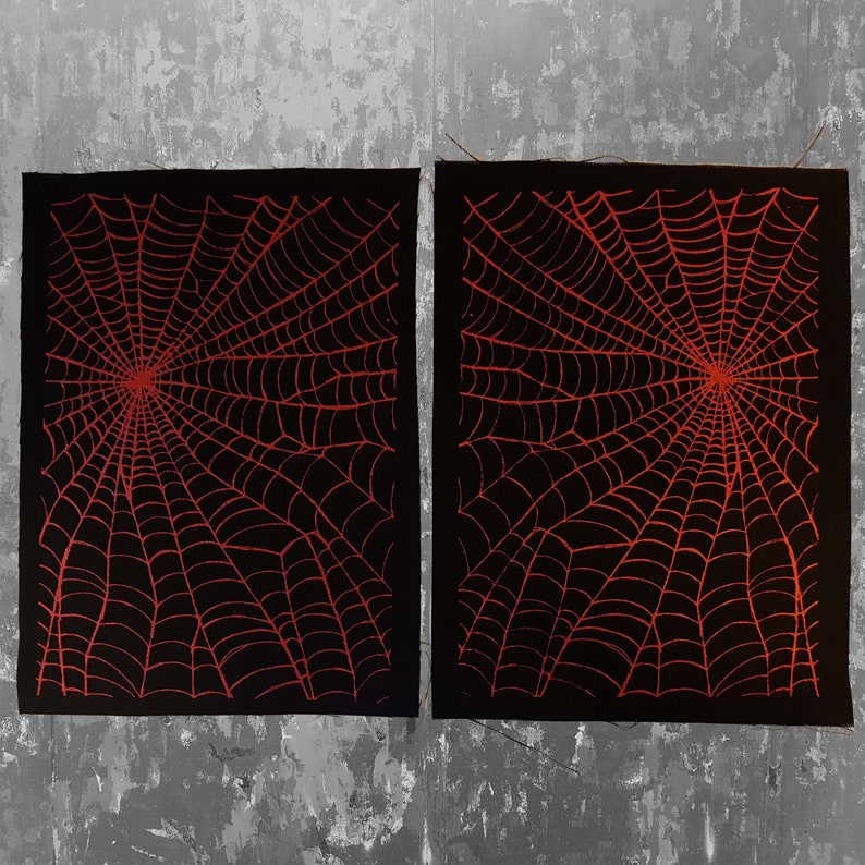 K&ouml;nnte beinhalten: Zwei schwarze Stoffbahnen mit einem roten Spinnennetz-Design. Die Bahnen liegen nebeneinander und haben eine raue Textur.