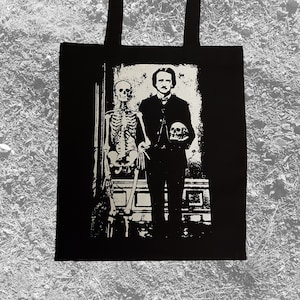 Può includere: Borsa tote in bianco e nero con una stampa grafica di Edgar Allan Poe in piedi accanto a uno scheletro che tiene un teschio.
