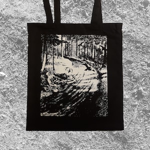 May include: Black tote bag with a white graphic print of a forest path with a figure walking through it.