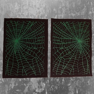 K&ouml;nnte beinhalten: Zwei schwarze Stoffbahnen mit einem gr&uuml;nen Spinnennetz-Design. Die Bahnen liegen nebeneinander und haben eine raue Textur.