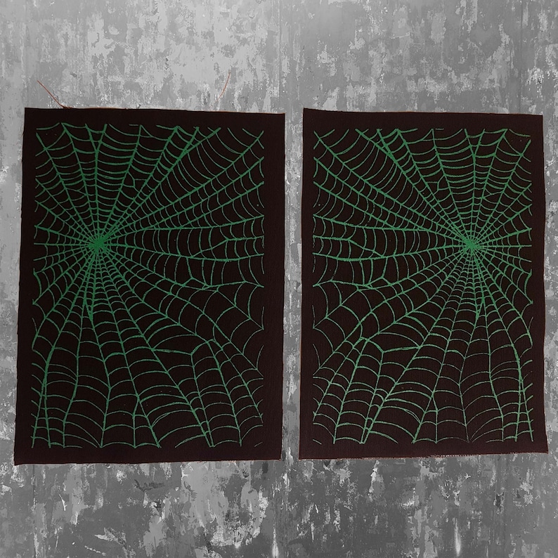 K&ouml;nnte beinhalten: Zwei schwarze Stoffbahnen mit einem gr&uuml;nen Spinnennetz-Design. Die Bahnen liegen nebeneinander und haben eine raue Textur.