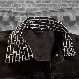 May include: A black denim jacket with a white brick pattern on the collar.