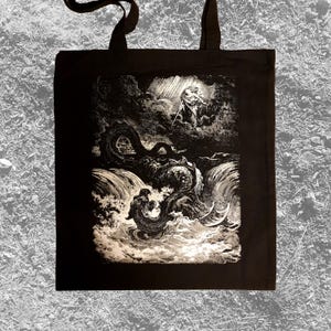 Op de afbeelding: Zwarte draagtas met een zwart-wit illustratie van een mythologische scène. Het kunstwerk toont een figuur in de wolken met een zwaard, een zeeslang en figuren in het water. De tas heeft twee zwarte handvatten.