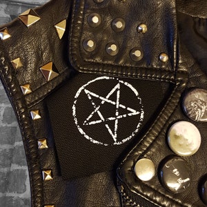 May include: A black leather jacket with silver studs and a white pentagram patch on the front.