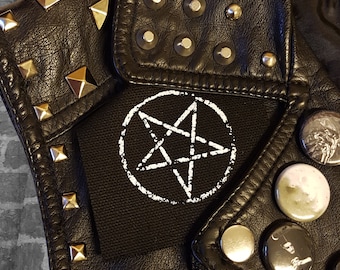 May include: A black leather jacket featuring silver pyramid studs on the shoulder, round silver studs on the lapel, and a black fabric patch with a white printed pentagram. The jacket is decorated with several circular pin-back buttons.