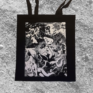May include: Black tote bag with a white print of a scene with multiple figures in a dark, fantastical setting.