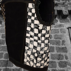 May include: A black denim vest with a white and black checkered pattern on the back. The vest has a frayed edge and is decorated with silver studs.