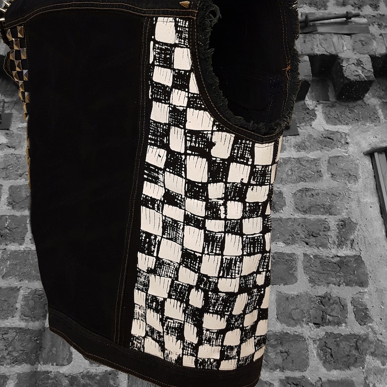 May include: A black denim vest with a white and black checkered pattern on the back. The vest has a frayed edge and is decorated with silver studs.