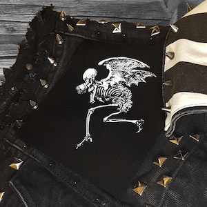 May include: Black denim jacket with silver pyramid-shaped studs and a white skeleton with wings patch sewn on the front.