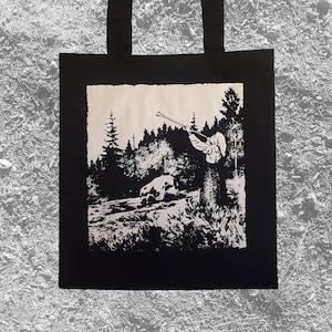 May include: Black and white tote bag with a graphic print of a person blowing a horn in a forest. The person is wearing a hat and a long coat. The forest is filled with trees and bushes.