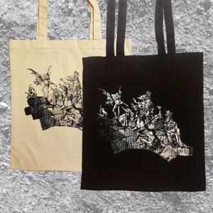 May include: Two tote bags with a black and white graphic print of a group of figures with wings and horns. The tote bag on the left is beige and the tote bag on the right is black.