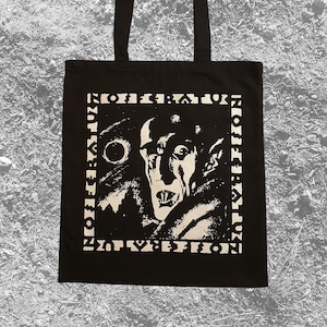 May include: Black tote bag with a white graphic of a vampire-like figure with the word "NOX:EFFECTION" in a border around the image. The bag has two black handles.